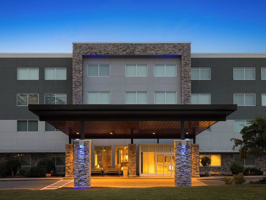 A modern hotel entrance with a covered walkway, stone facade, and large windows.