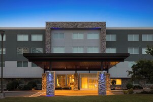 Una entrada de hotel moderna con un vestíbulo cubierto, fachada de piedra y amplias ventanas.