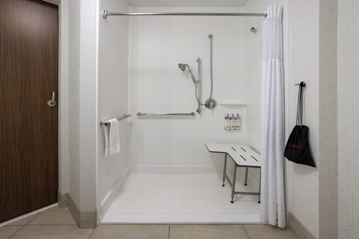 A walk-in shower with a glass door, a handrail, a small bench, and a towel rack.