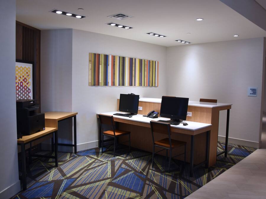 A hotel workspace with two desks, chairs, computers, and a wall-mounted artwork.