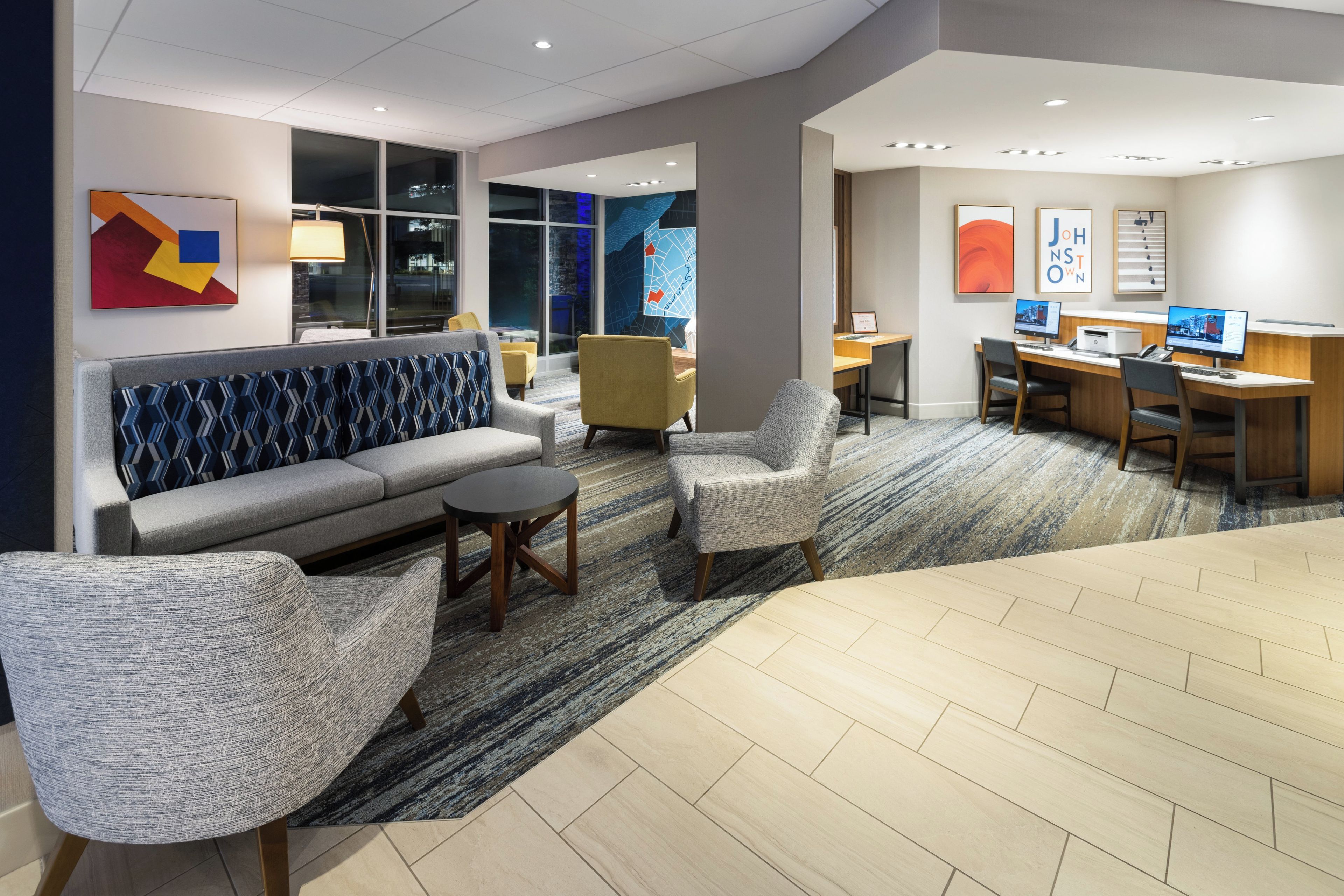 A modern hotel lobby with a sofa, armchairs, a small table, and a reception desk.