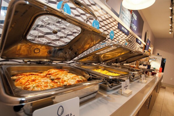 Buffet com diversas opções de comida, incluindo ovos mexidos e um prato de pizza.