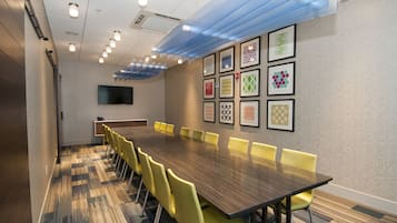 Une salle de conférence avec une longue table, des chaises jaunes et des œuvres d’art encadrées accrochées au mur.