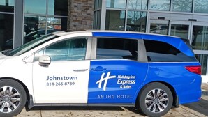 A white and blue van with "Johnstown" and "Holiday Inn Express & Suites" branding parked in front of a building.