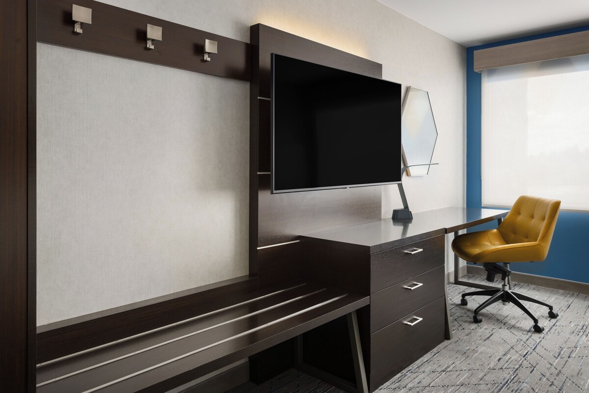 A modern office space with a dark wooden desk, a flat-screen monitor, and a yellow office chair.
