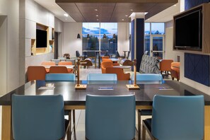 A modern conference room with a large table, blue and orange seating, and large windows offering a view of the outdoors. - Holiday Inn Express & Suites Johnstown by IHG (Johnstown)