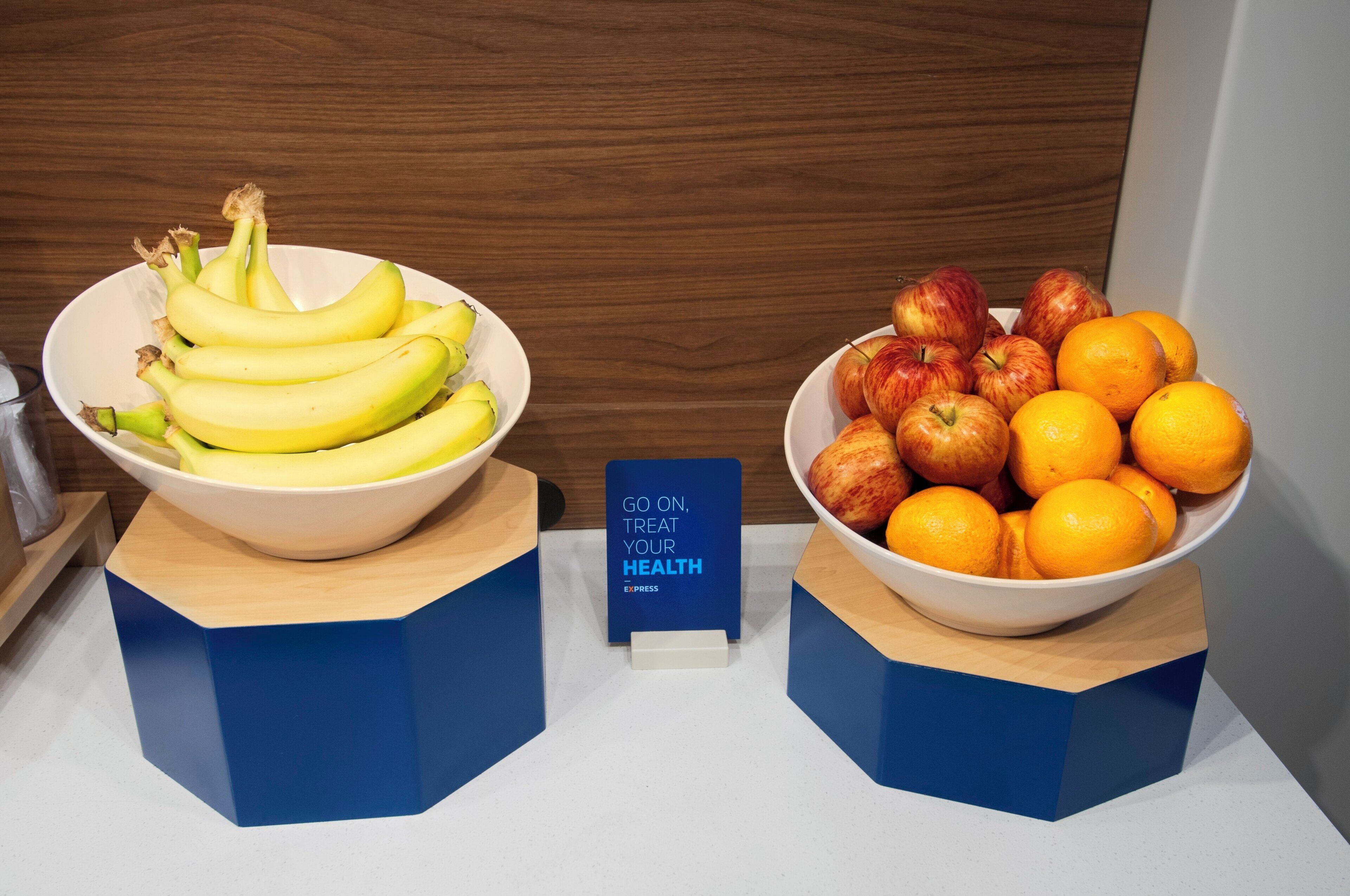 Two bowls of fruit on a counter with a sign that reads 'GO ON, TREAT YOUR HEALTH'.