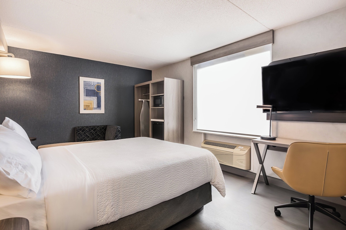 A hotel room with a bed, a desk, a television, a wardrobe, and a window.