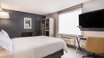 Una habitación de hotel con una cama, un escritorio, un televisor, un armario y una ventana.