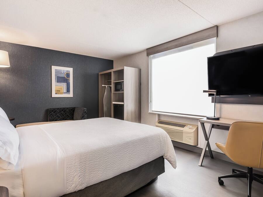 Una habitación de hotel con una cama, un escritorio, un televisor, un armario y una ventana.