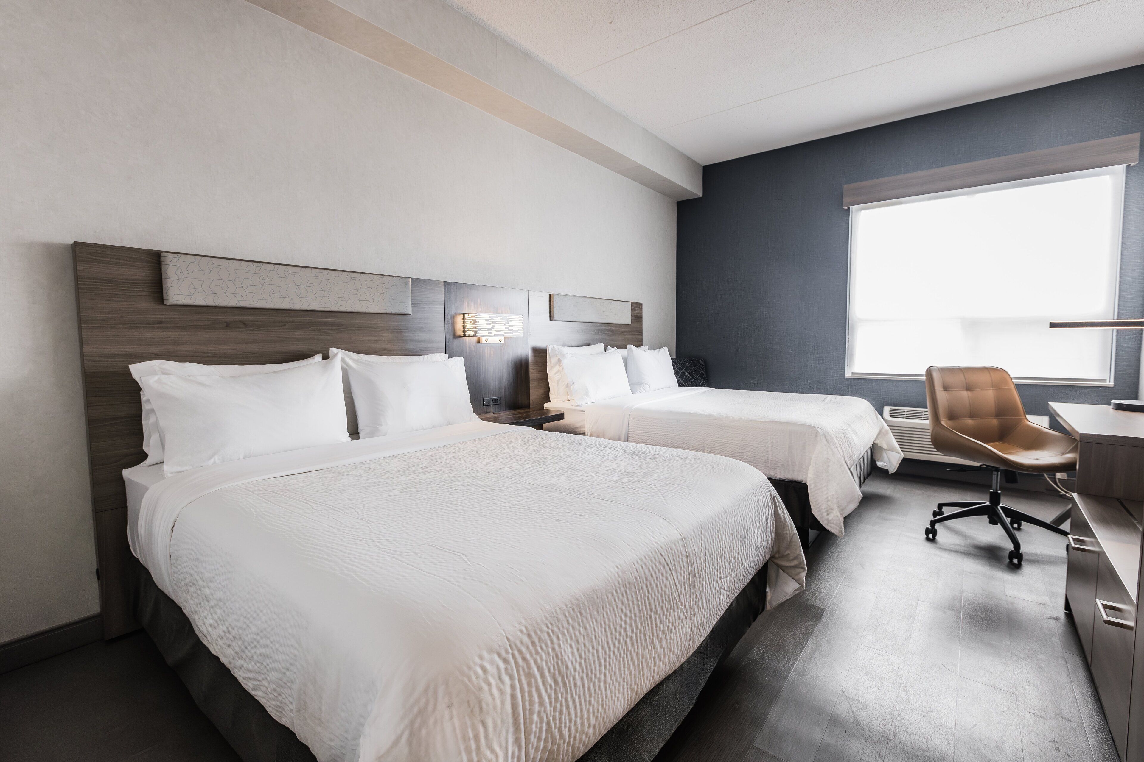 A hotel room with two beds, a desk, a chair, and a large window.