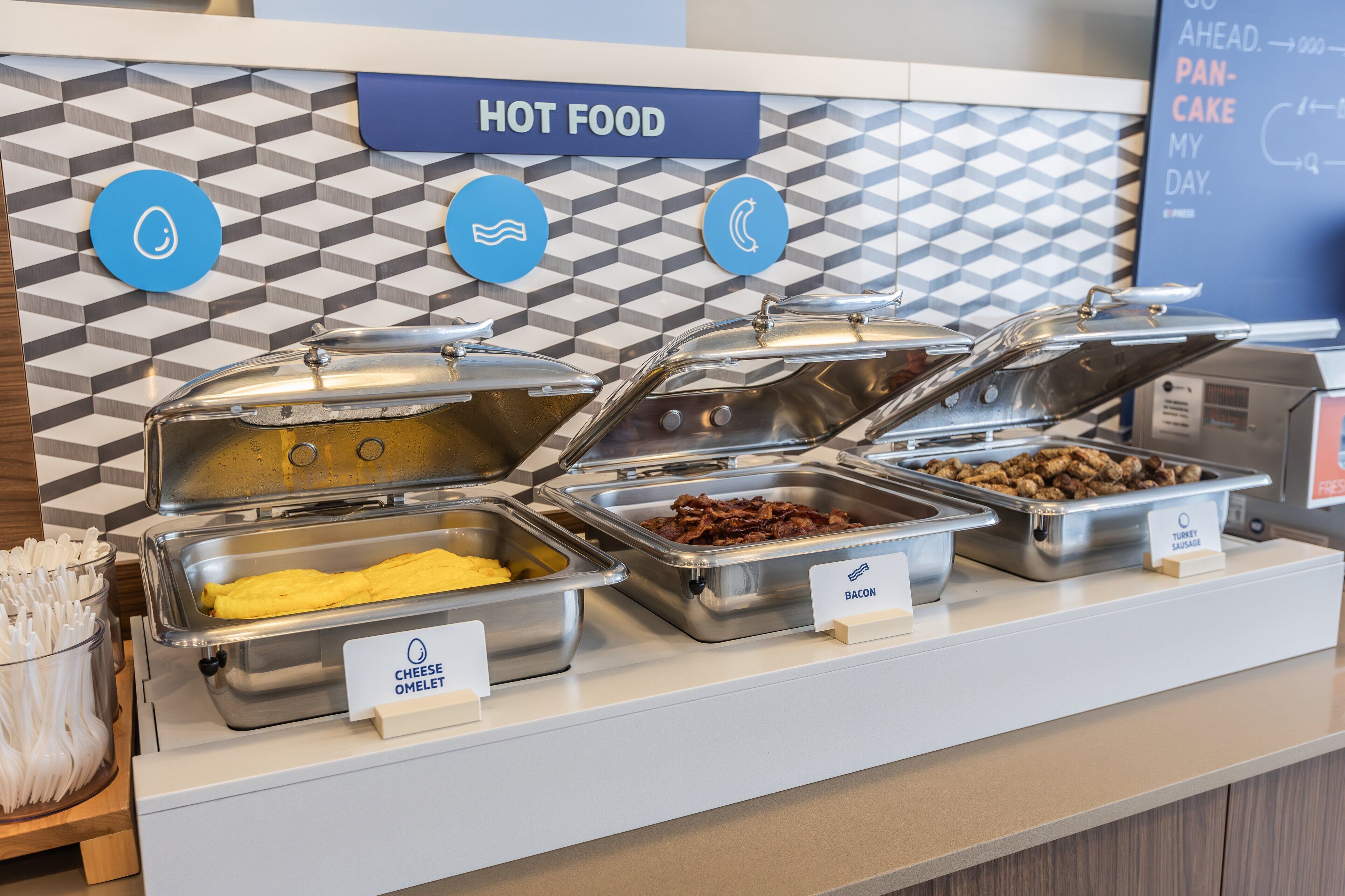 Un buffet proposant différents plats, chacun étant clairement identifié, notamment des omelettes, du bacon et des saucisses de dinde.