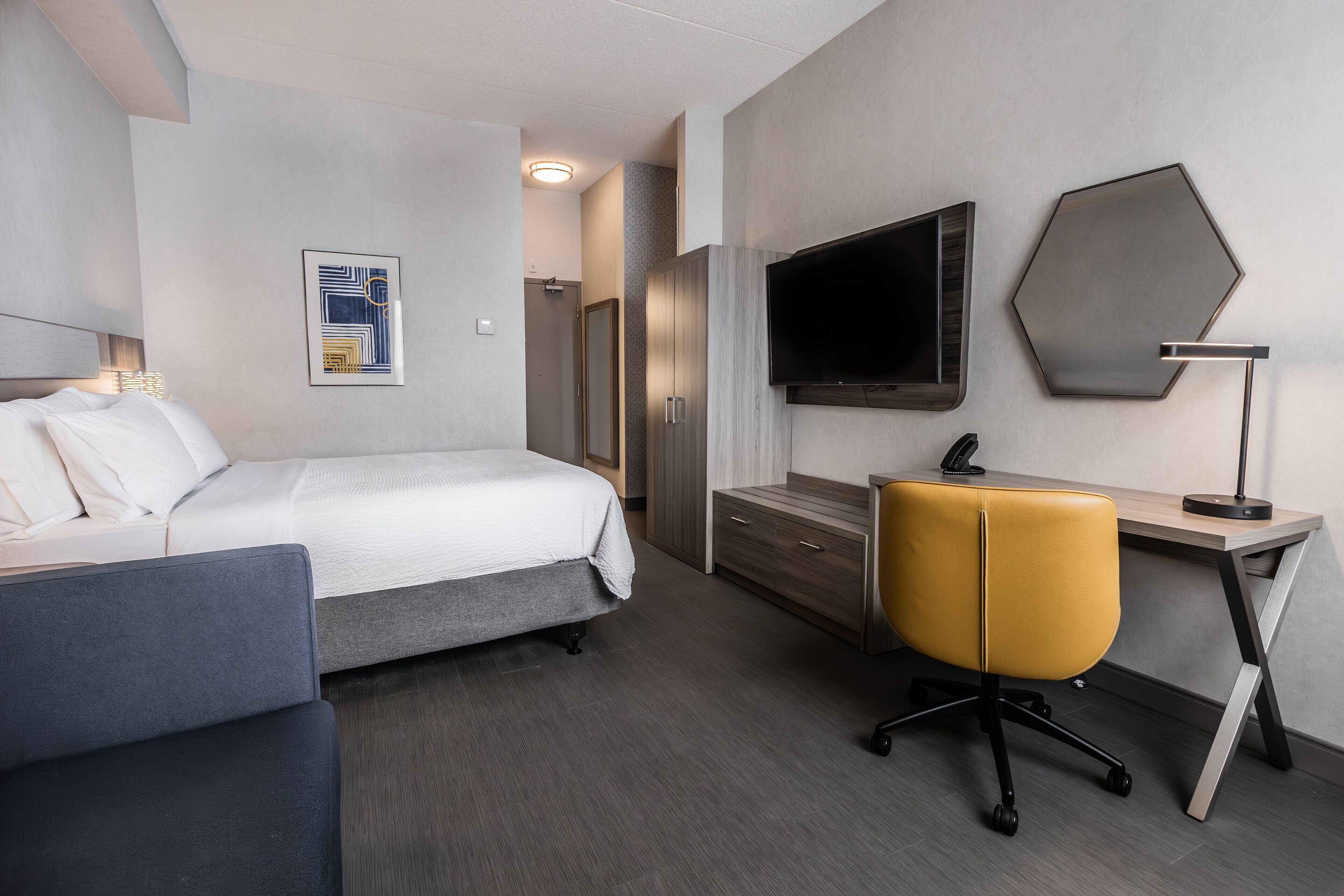 A modern hotel room with a bed, a desk, a chair, a TV, and a wardrobe.