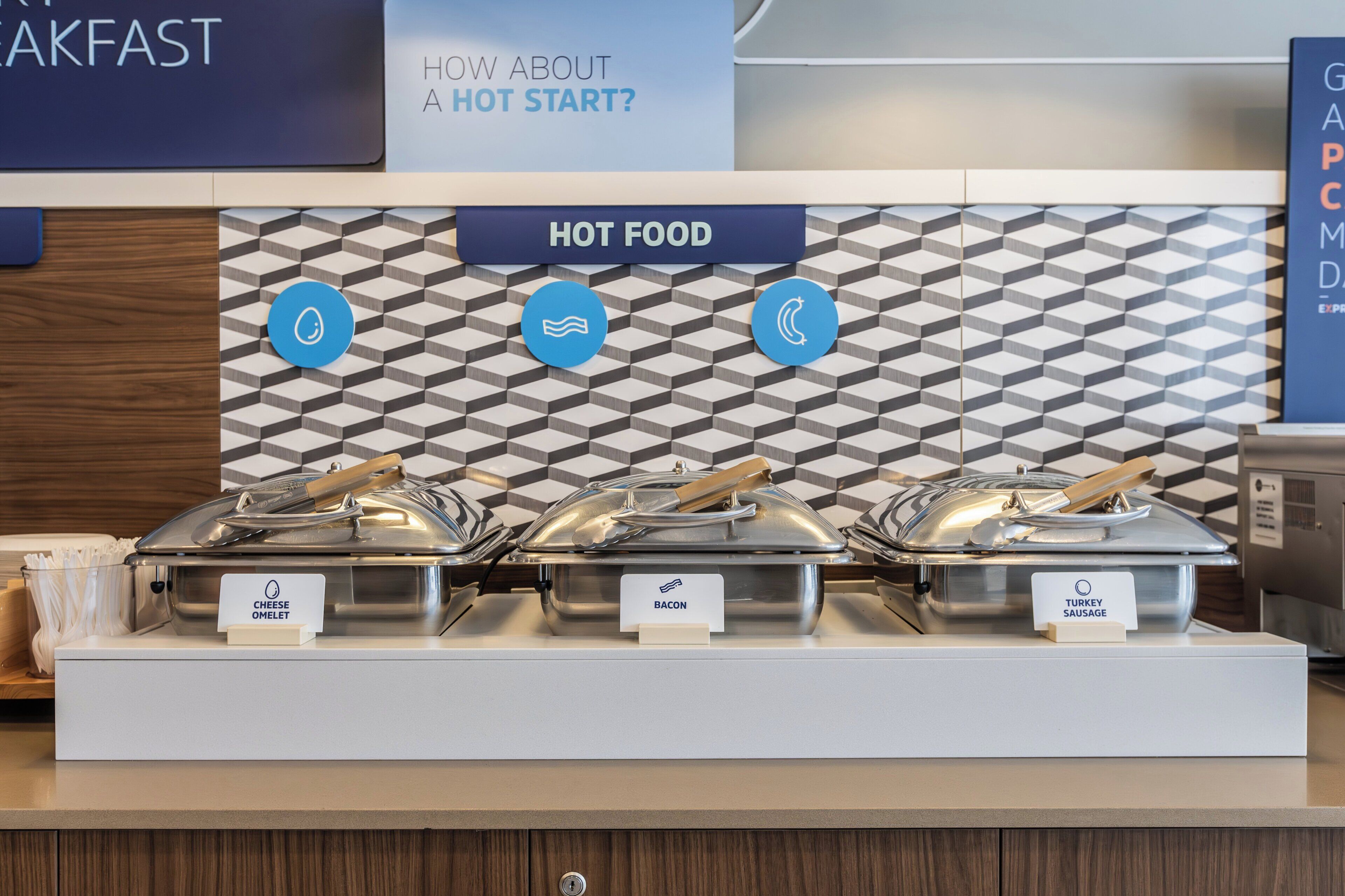 A buffet area with labeled hot food options including cheese omelet, bacon, and turkey sausage.