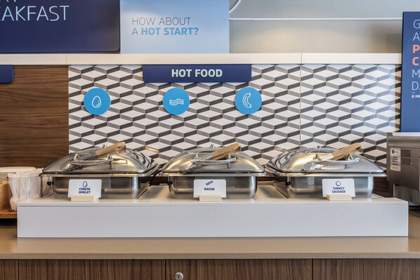 A buffet area with labeled hot food options including cheese omelet, bacon, and turkey sausage.