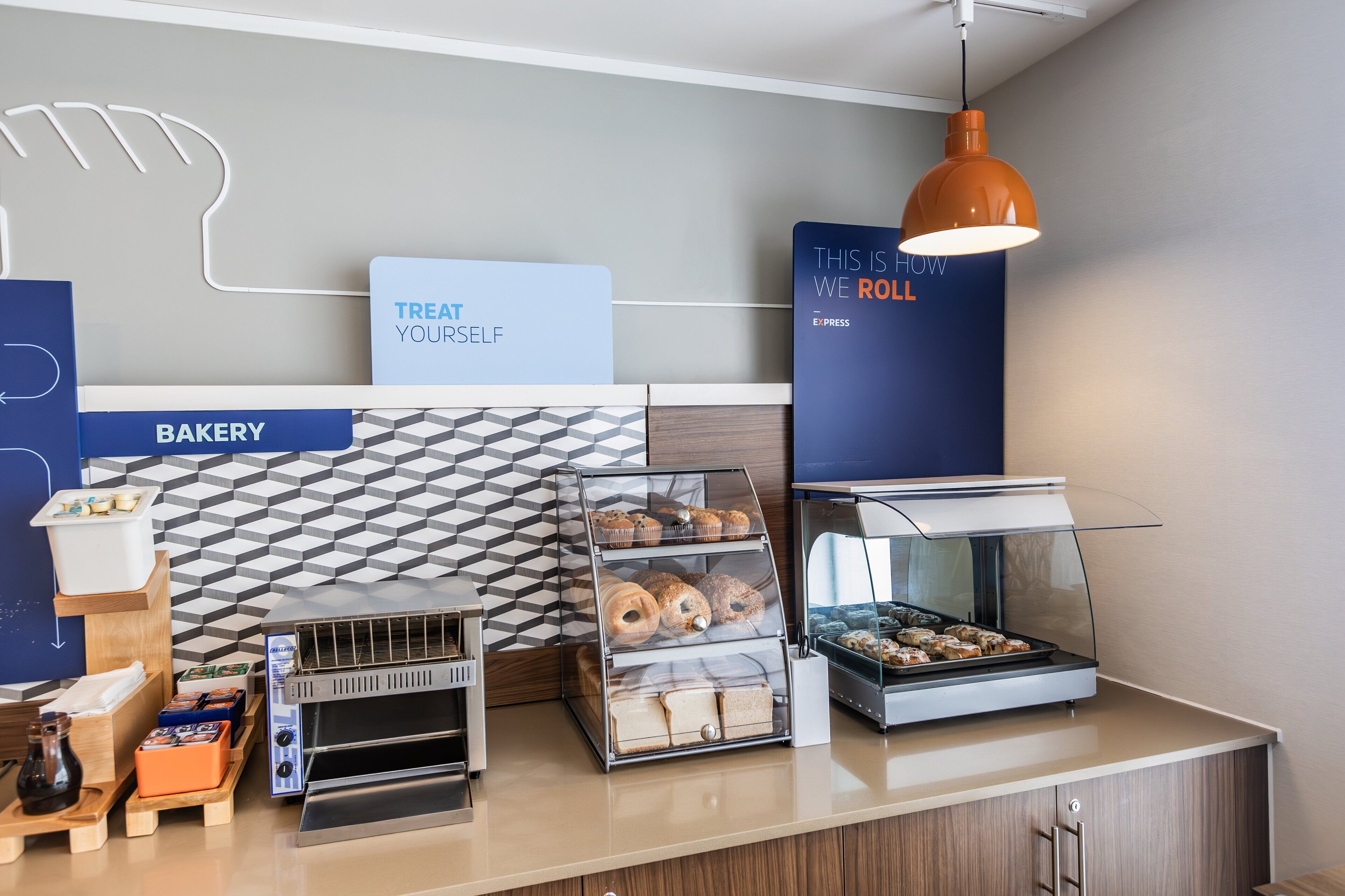 A bakery counter with a display case, a toaster, and a sign that says "THIS IS HOW WE ROLL".