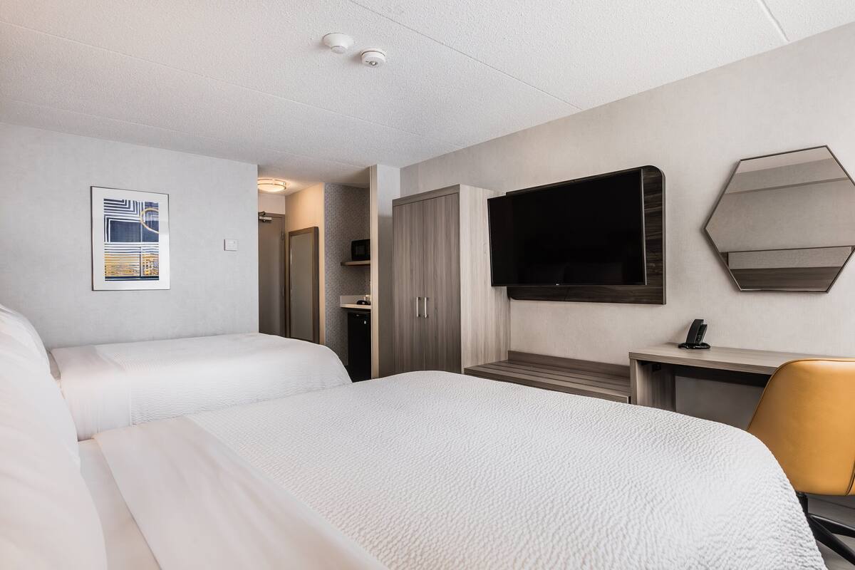 A hotel room with two beds, a desk, a chair, a TV, and a wardrobe.