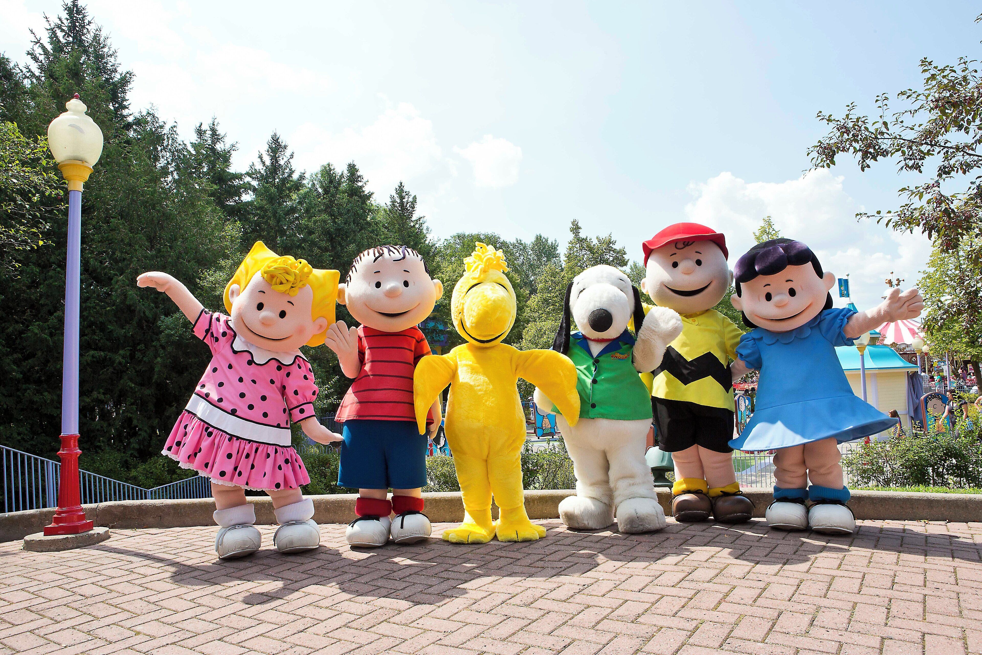 A group of cartoon character statues standing on a paved area with trees and a lamp post in the background.