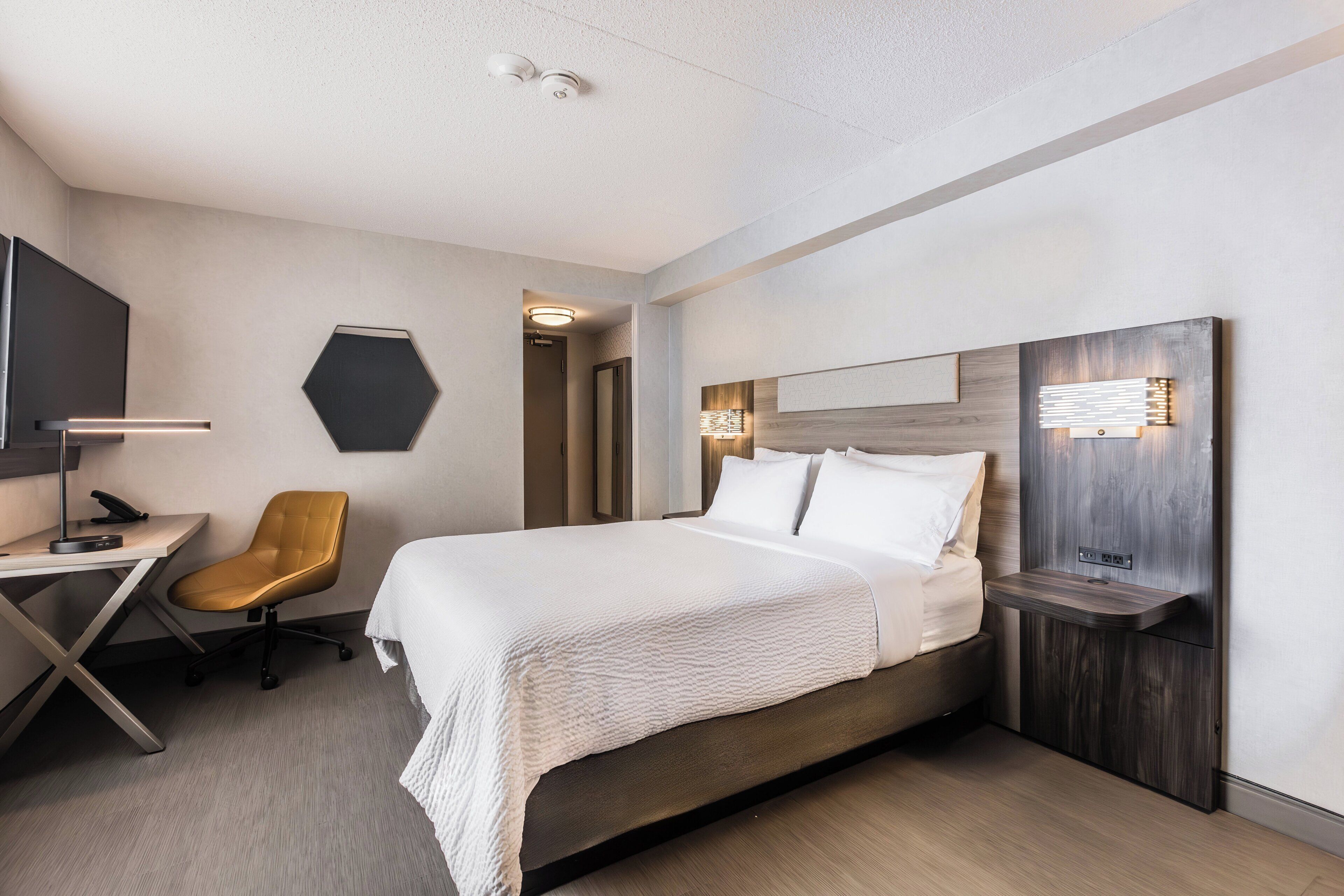 A modern hotel room with a bed, desk, chair, and a TV.