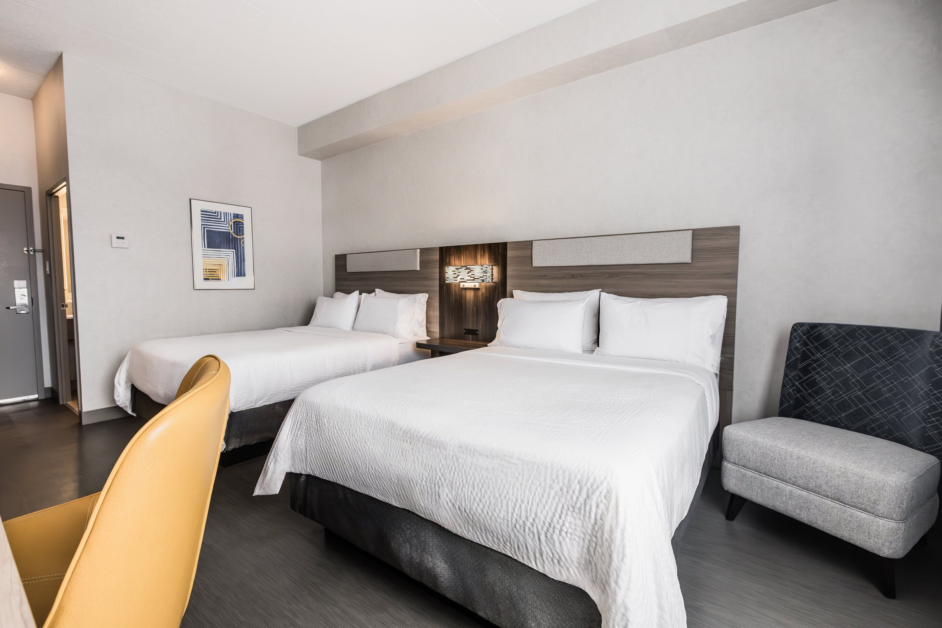 A hotel room with two beds, a chair, and a nightstand.