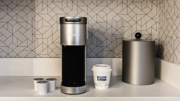 Cozinha moderna com uma cafeteira elegante, uma xícara de café e um recipiente cilíndrico em uma bancada branca.