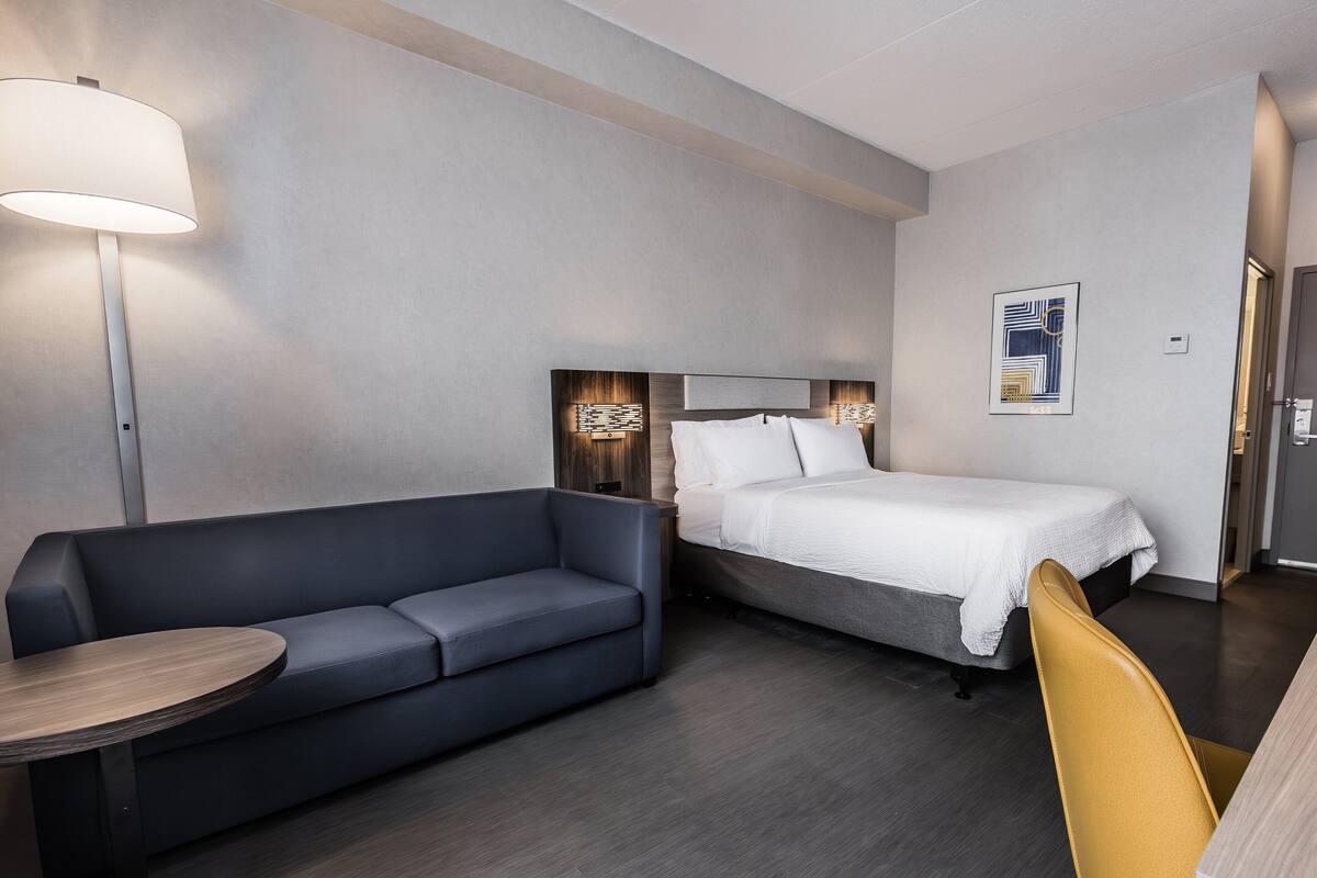 A modern hotel room with a sofa, a bed, a small table, and a chair.