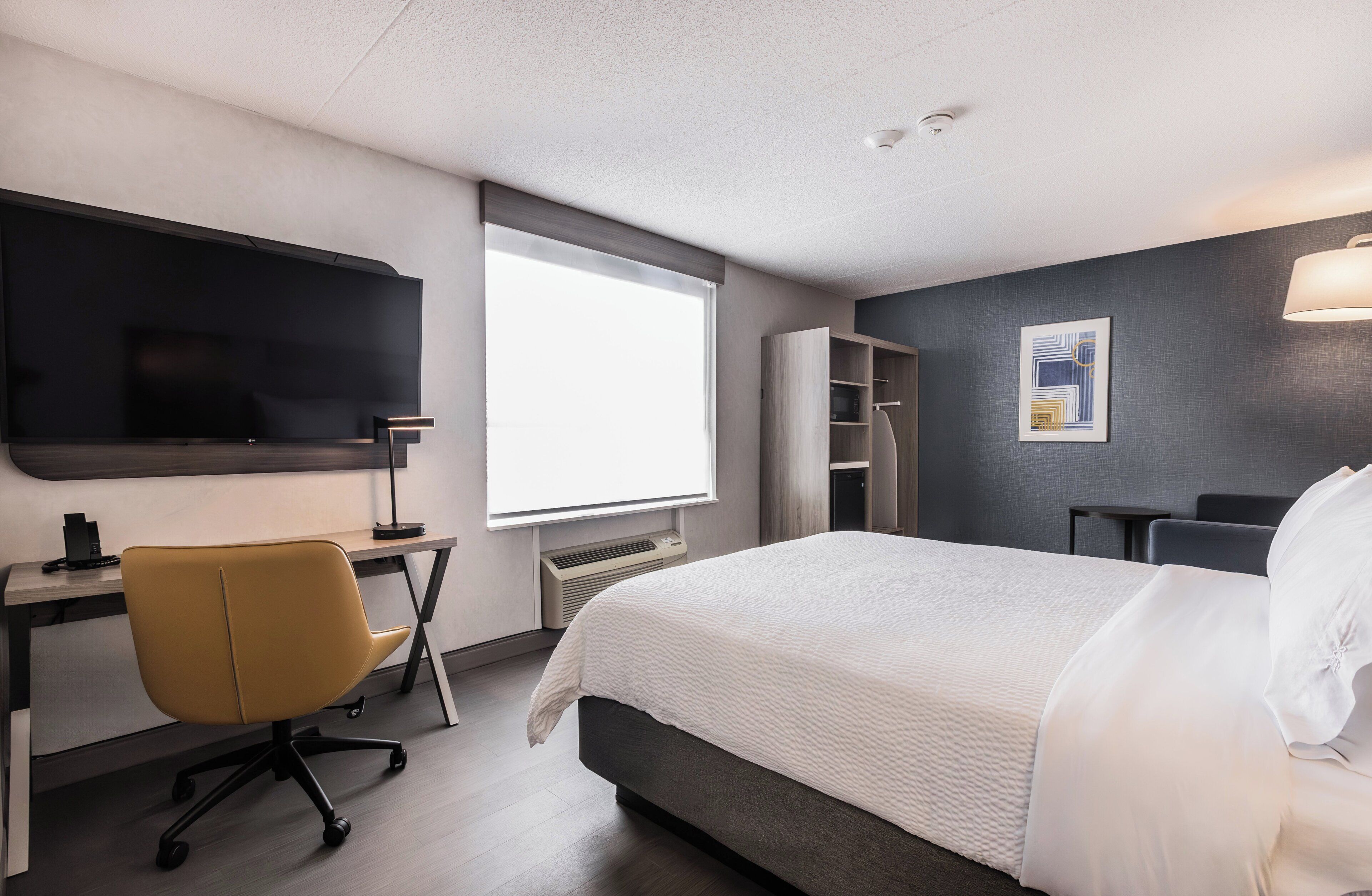 Una habitación de hotel con cama, escritorio, silla y televisor de pantalla plana.