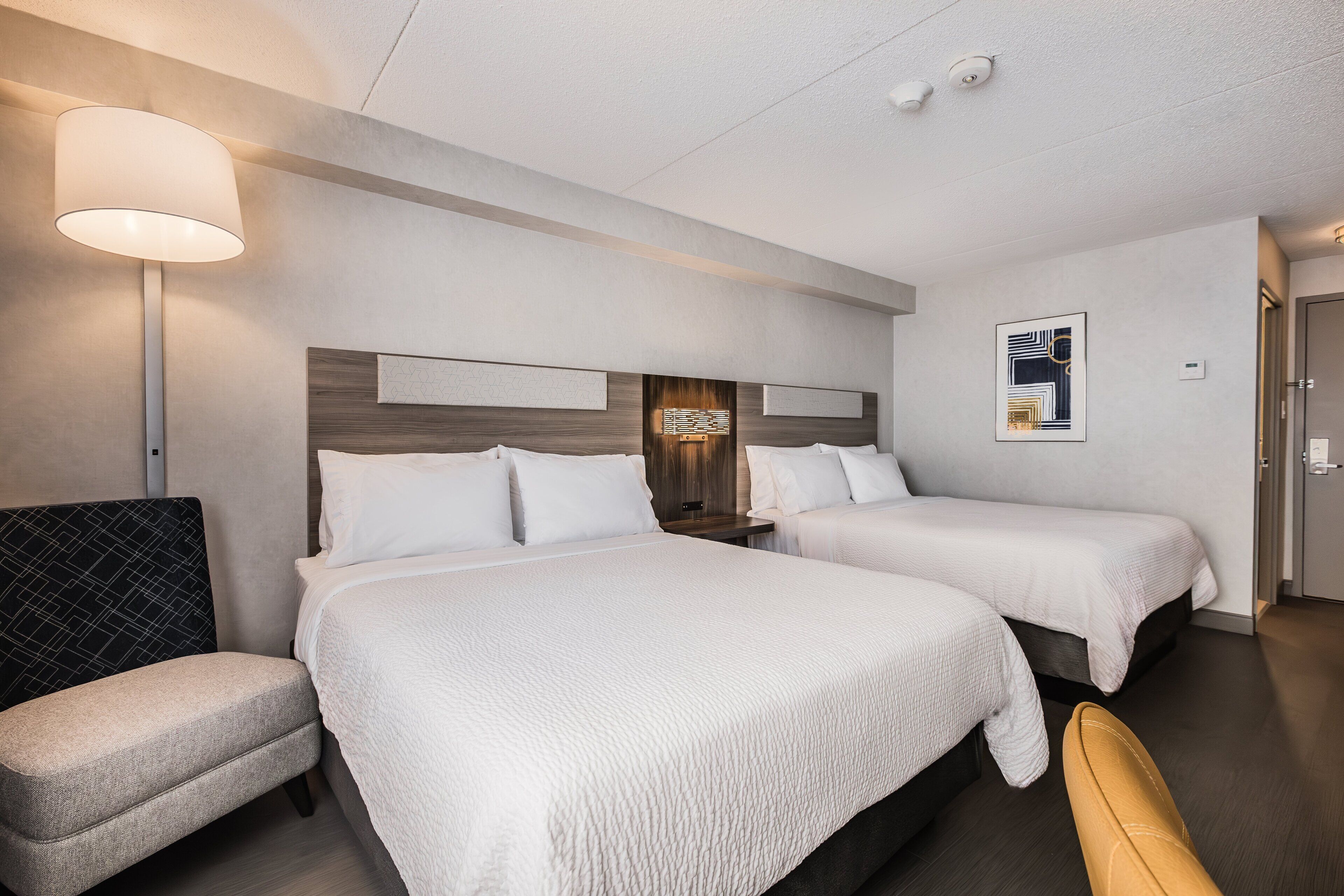 Une chambre d’hôtel avec deux lits, un canapé, une lampe et une œuvre d’art accrochée au mur.