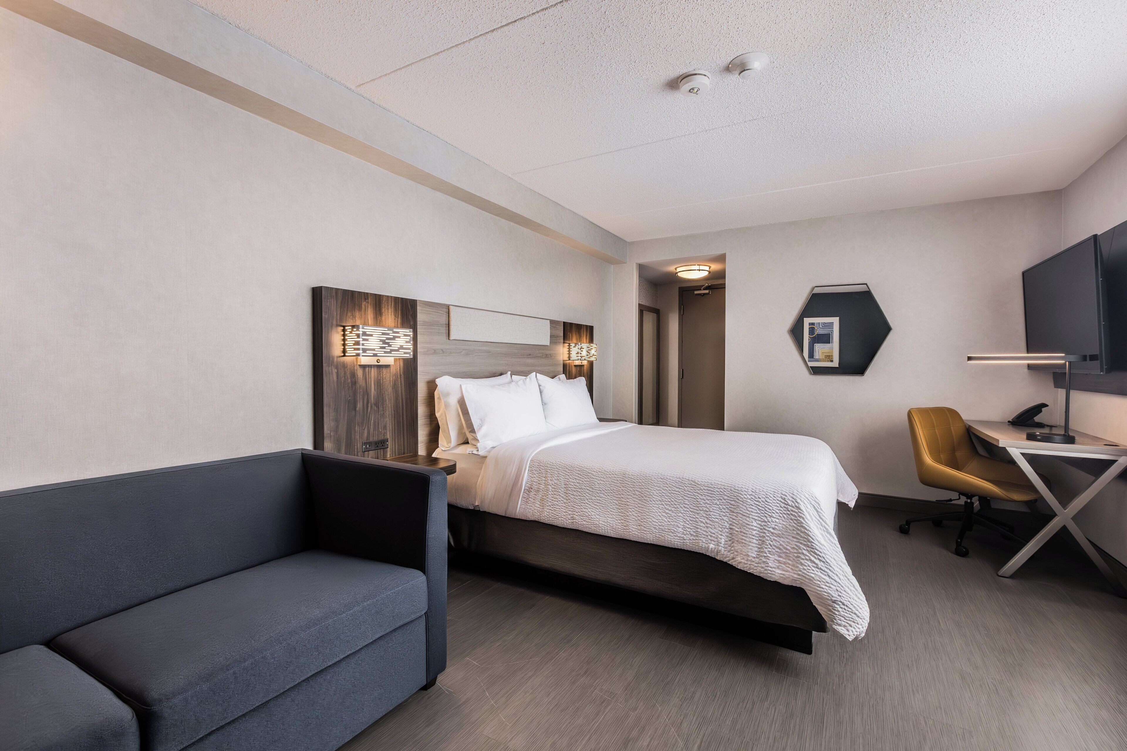 A hotel room with a bed, a desk, a chair, and a television.