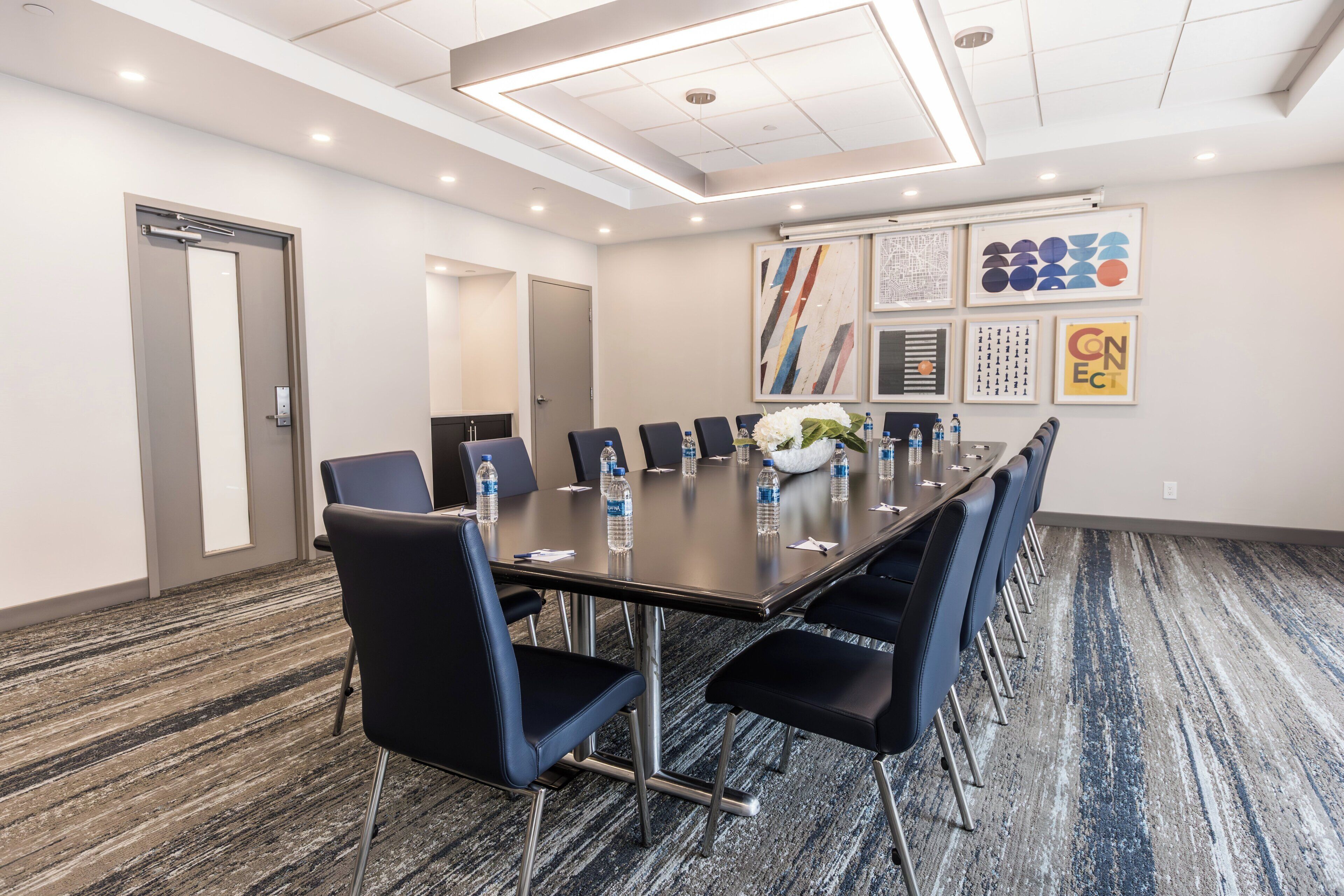 A conference room with a long table, chairs, water bottles, and framed artwork on the walls.