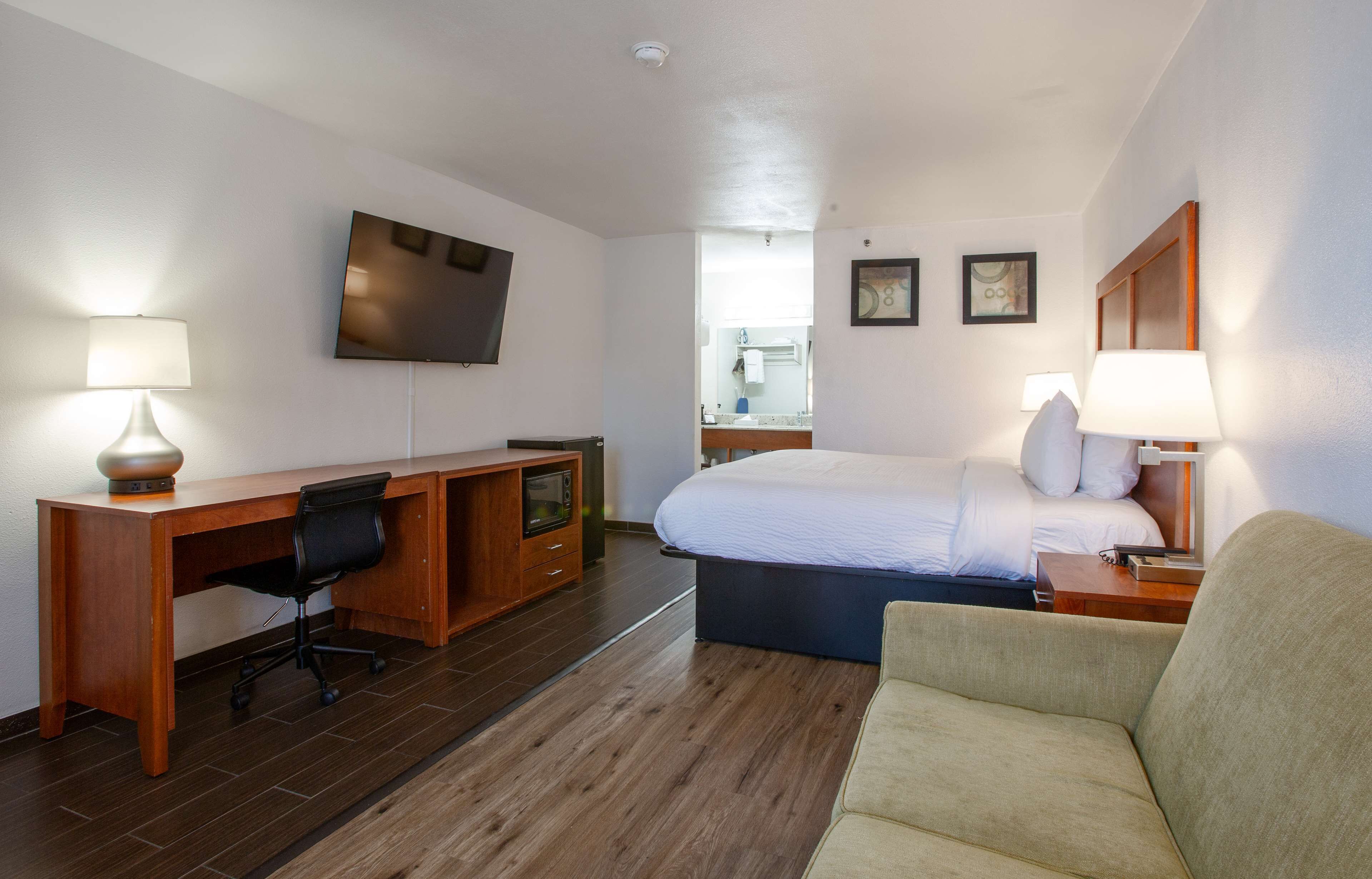A hotel room with a bed, a desk with a chair, a TV mounted on the wall, and a sofa.