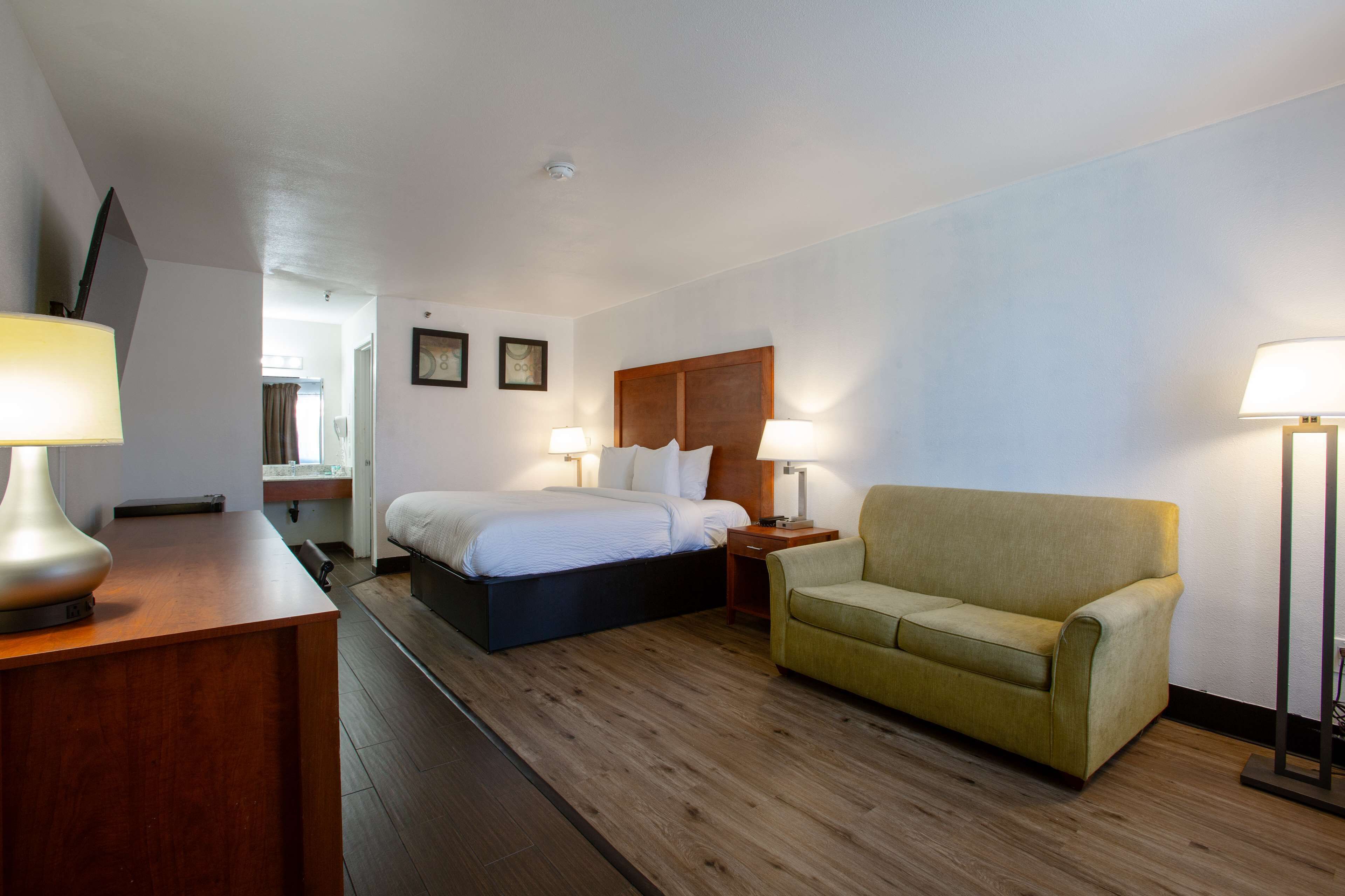A hotel room with a bed, a sofa, a desk with a lamp, and bedside lamps.