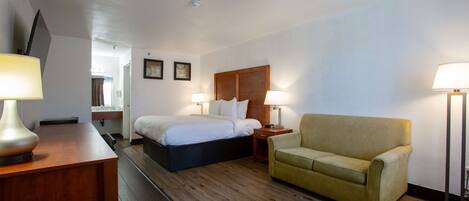 A hotel room with a bed, a sofa, a desk with a lamp, and bedside lamps.