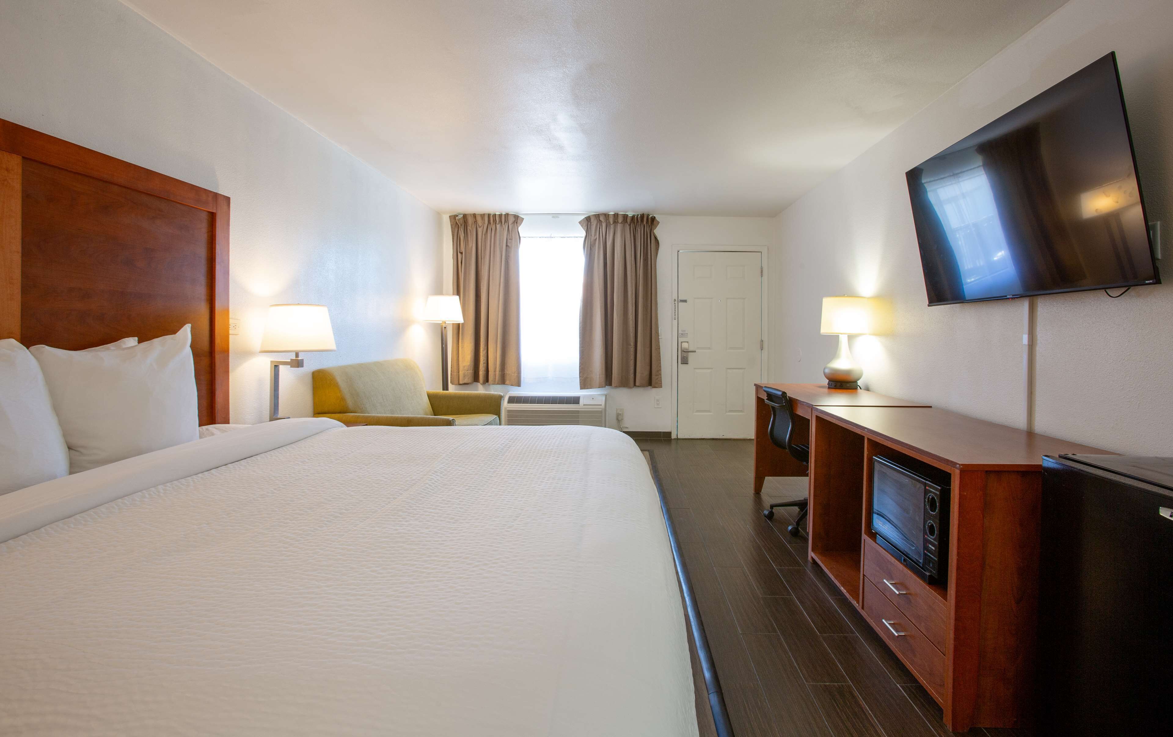 Una habitación de hotel con una cama grande, un escritorio con silla, un televisor y una lámpara de escritorio.