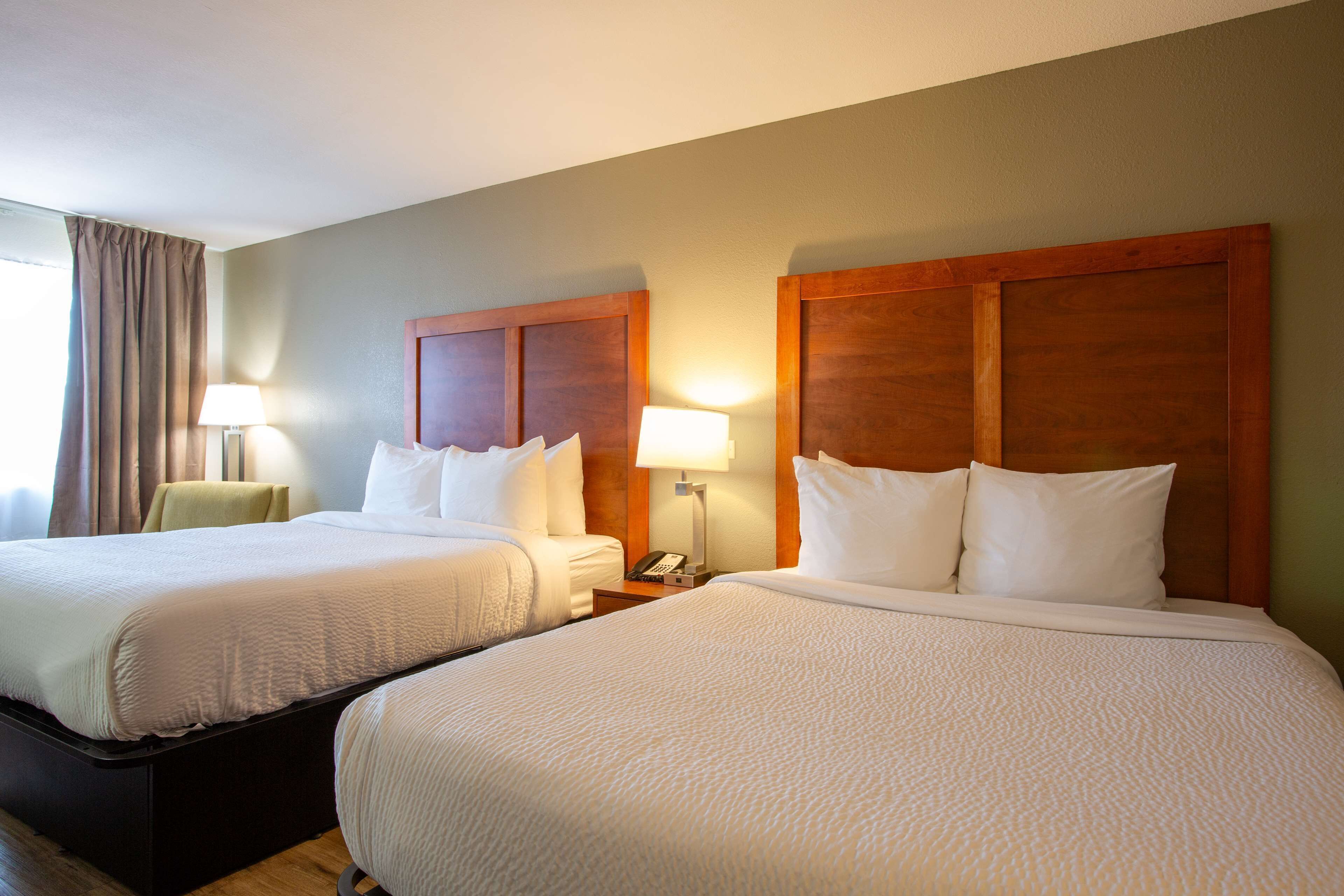 A hotel room with two beds, each with a wooden headboard, white bedding, and bedside lamps.