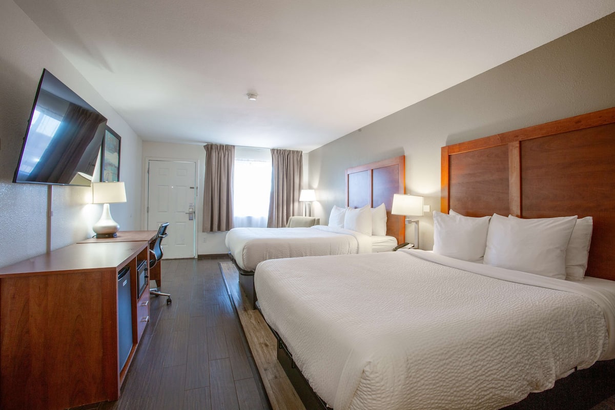 A hotel room with two beds, a desk with a TV, and a bathroom.