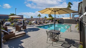 A pool area with lounge chairs and umbrellas, a pool, and a building in the background. - The Hotel Serene Glendale Peoria, Surestay Collection by BW (Glendale)