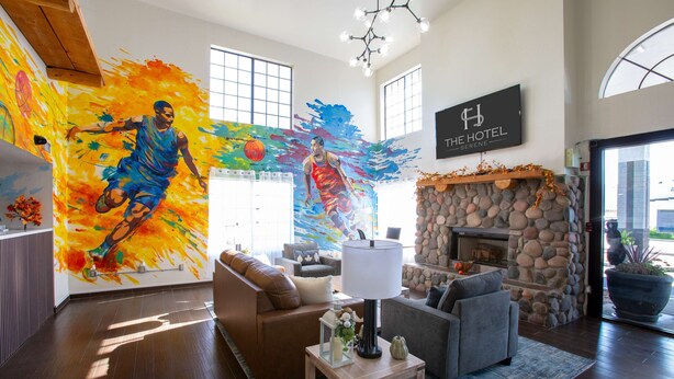 A spacious living room with a stone fireplace, a large mural on the wall, and a sign that reads "The Hotel Serenity." - The Hotel Serene Glendale Peoria, Surestay Collection by BW (Glendale)