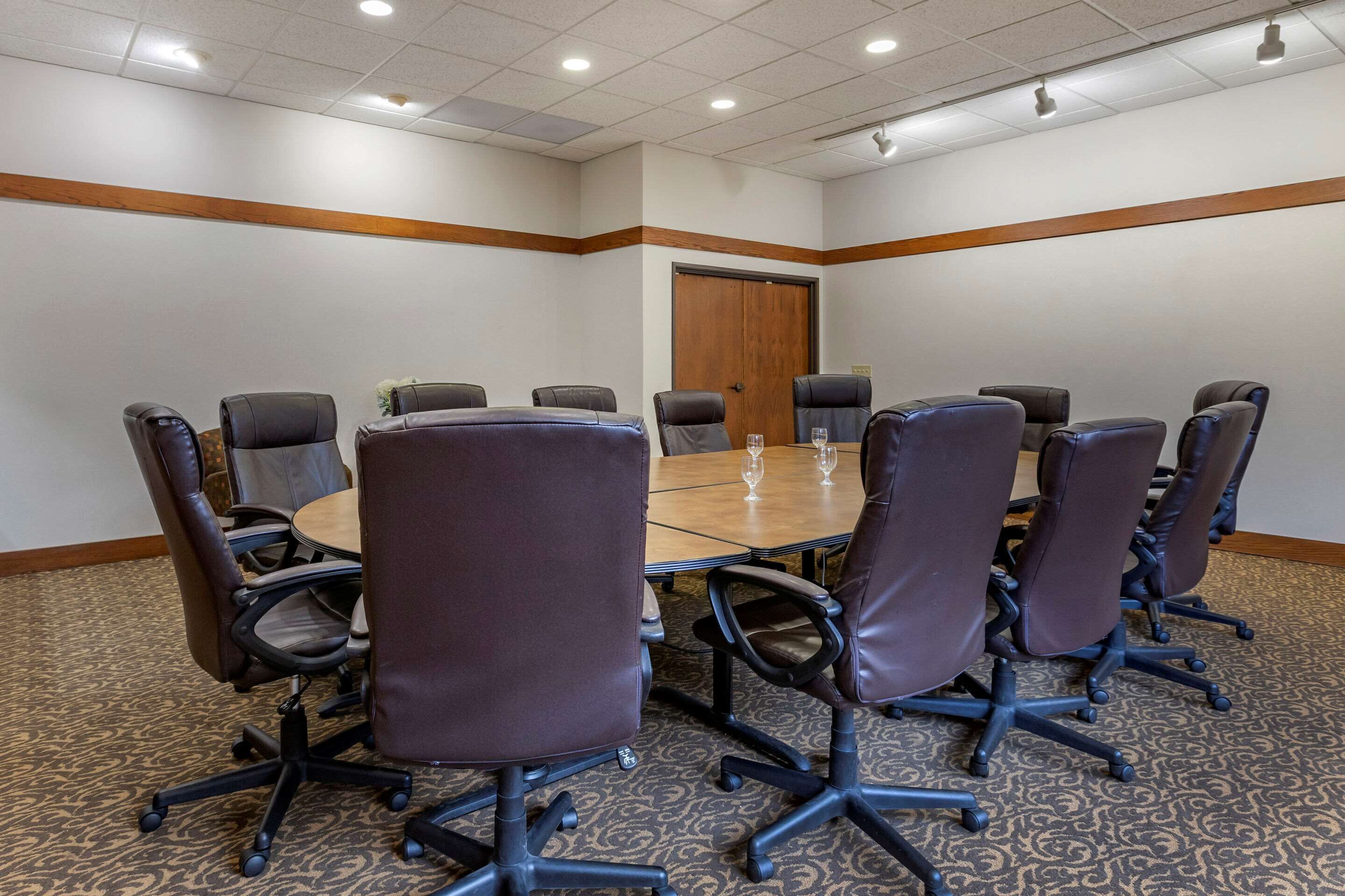Une salle de conférence dotée d’une grande table ovale, de huit fauteuils en cuir et d’une porte en bois.