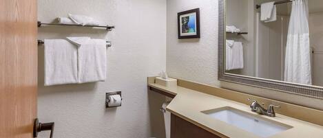 A bathroom with a toilet, sink, and mirror. There are towels on a shelf and a picture on the wall.