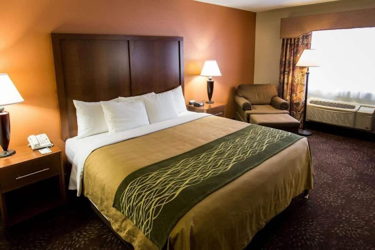 A hotel room with a large bed, two bedside tables, a chair, a desk, and an air conditioning unit.