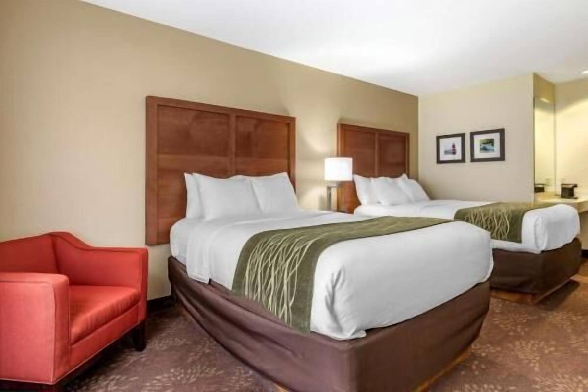 A hotel room with two beds, a red armchair, and a wooden headboard.
