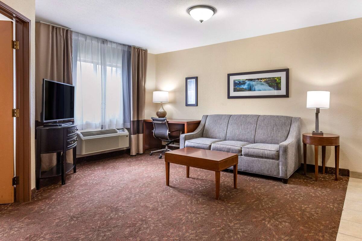 A hotel room with a sofa, a desk, a television, and a lamp.