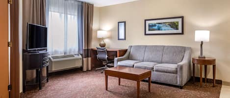 A hotel room with a sofa, a desk, a television, and a lamp.