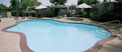 A swimming pool with a brick border, lounge chairs, and umbrellas.