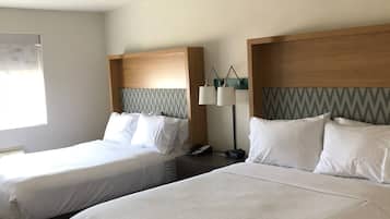Habitación de hotel con dos camas, una mesita de noche, una lámpara y un ventanal con un diseño geométrico en la pared.