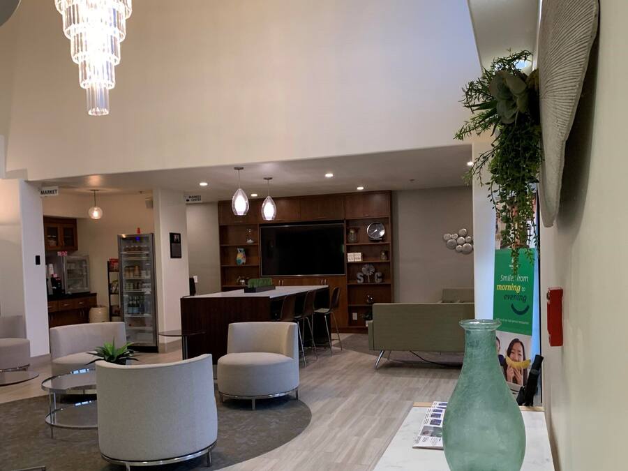 A spacious lobby with a chandelier, seating area, and a reception desk with a vase and newspapers.