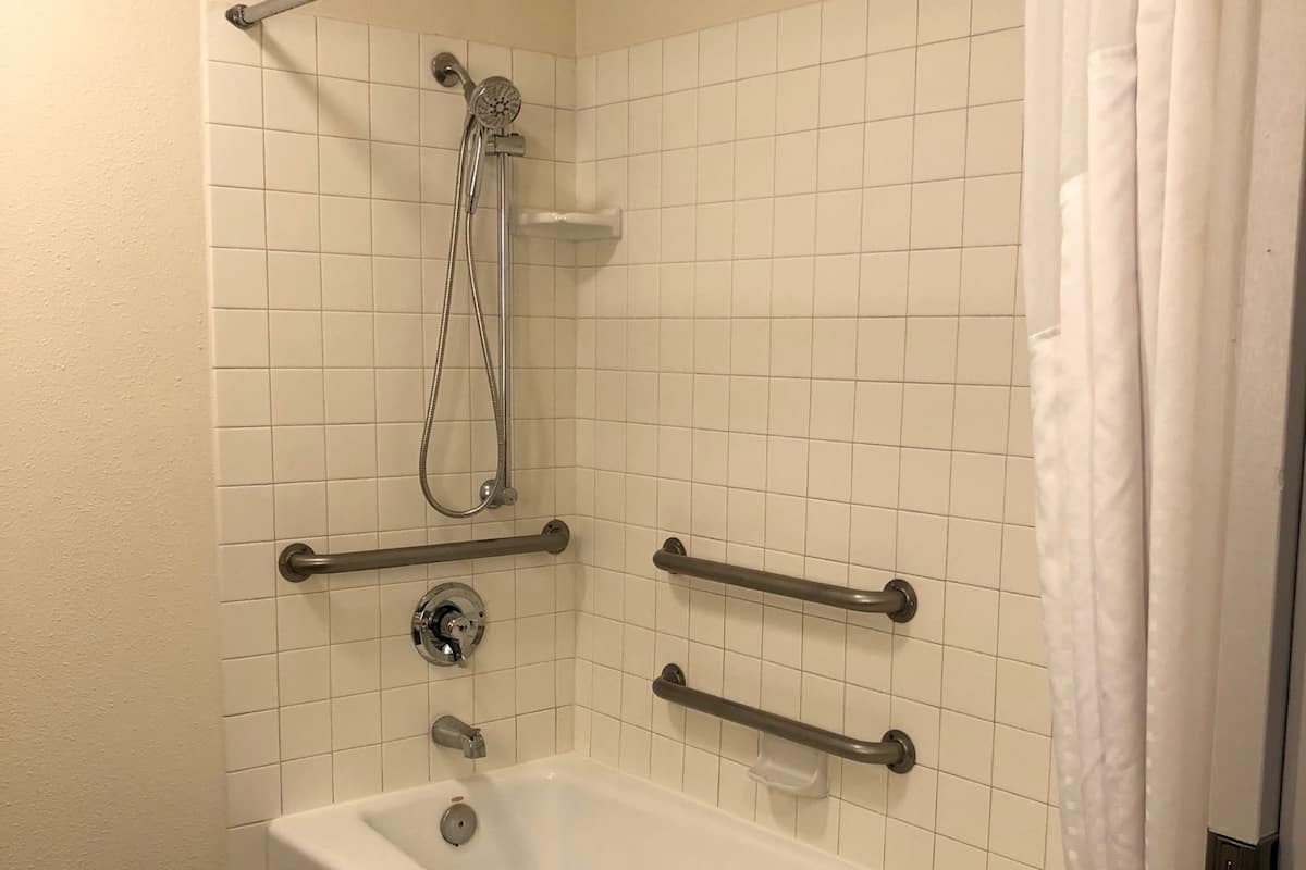 Ein Badezimmer mit einer weißen Badewanne, Haltegriffen, einer Duschbrause und einem Handtuchhalter.