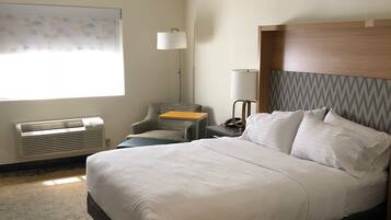 Habitación de hotel con una cama grande, un escritorio con lámpara, una silla y una ventana con persianas.