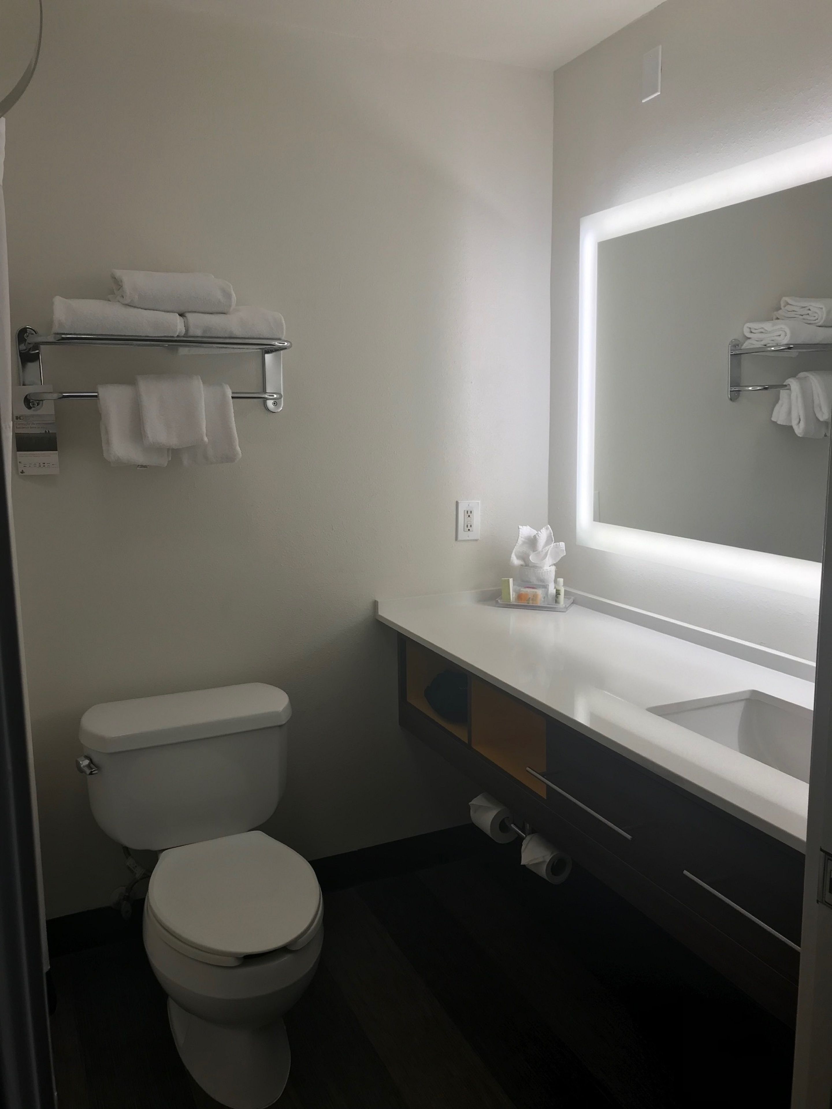 A compact bathroom with a toilet, a sink, a mirror, and towel racks.